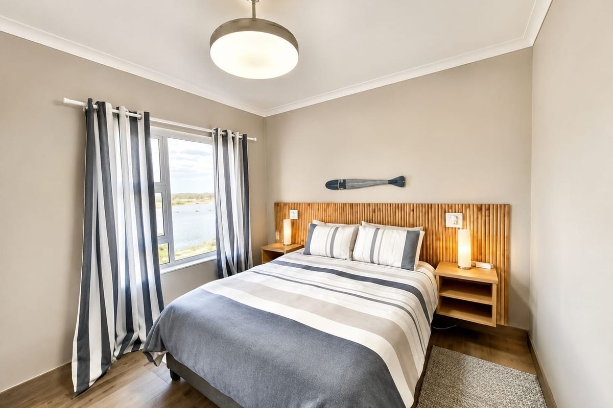 A well-maintained bedroom featuring a custom wooden headboard, laminate flooring, and a window with views of the surrounding landscape.