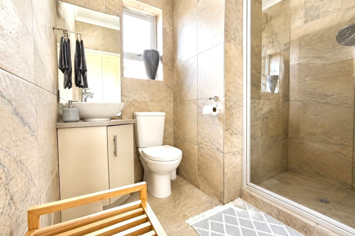 A modern bathroom featuring floor-to-ceiling stone-look tiling, a glass-enclosed shower, a vessel sink vanity, and a toilet.