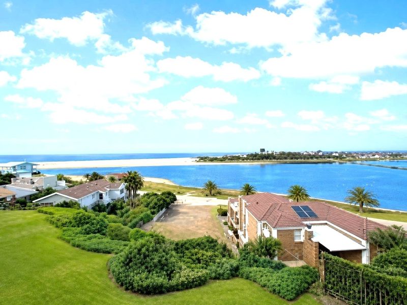 Elevated scenic view overlooking the coastal lagoon, sandy beach, and surrounding residential properties with clear blue skies.