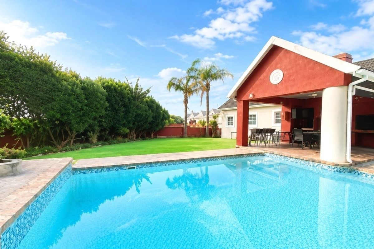 A well-maintained outdoor area featuring a sparkling swimming pool, a spacious covered patio with brick pillars, and a lush, manicured garden.