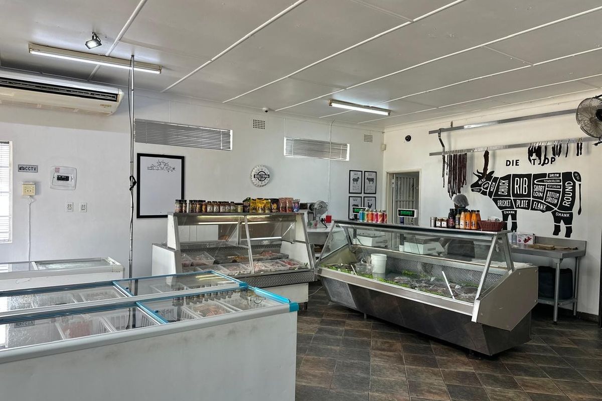 A functional retail butchery space featuring commercial refrigerated display counters, chest freezers, and tiled flooring, suitable for food service operations.