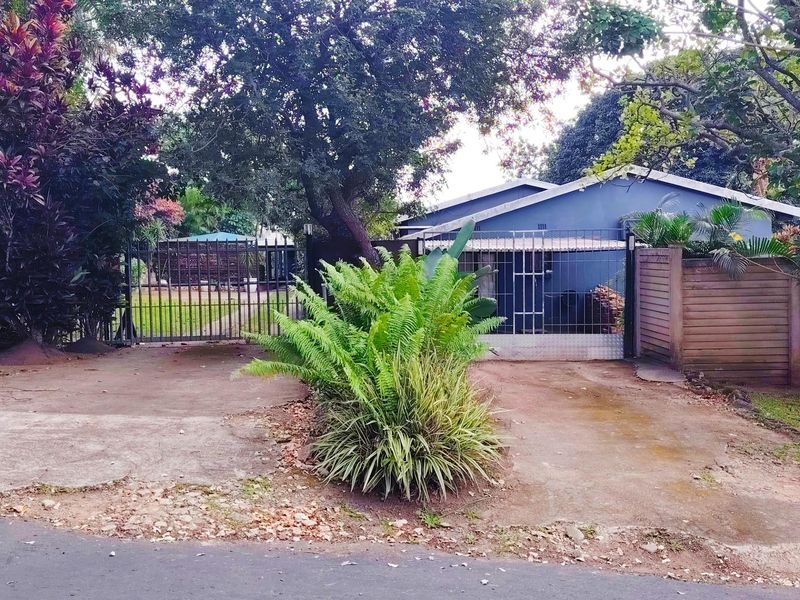 Front view of the property featuring a gated driveway entrance, concrete paving, and established garden surroundings.