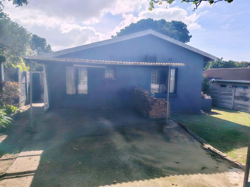 Rear view of the property featuring a covered carport, concrete driveway, and surrounding precast boundary walls in a residential setting.