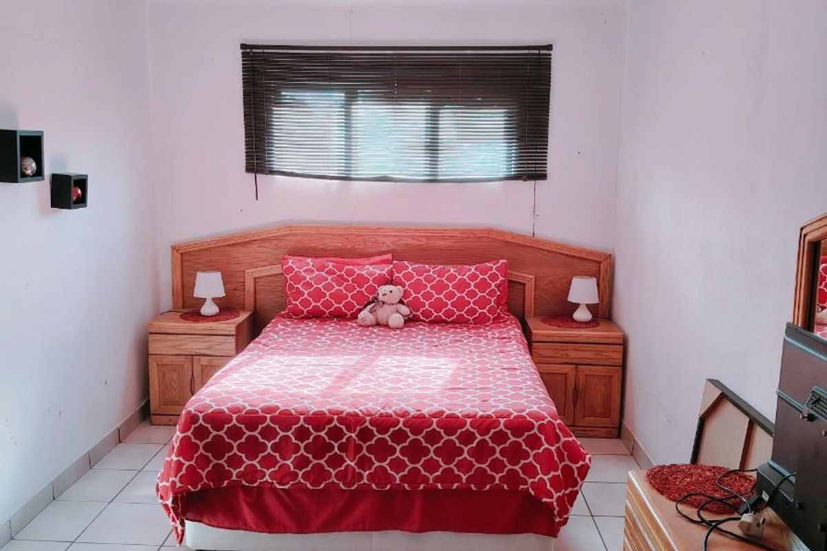 A bedroom featuring tiled flooring, a built-in wooden headboard with integrated bedside tables, and venetian blinds.