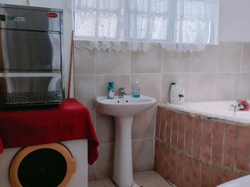 A functional bathroom featuring a pedestal basin, tiled bathtub, and toilet, with neutral wall and floor tiling throughout.