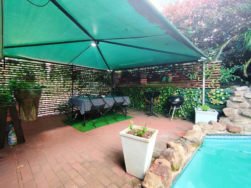 Outdoor pool area featuring brick paving, a rockery border, and a green shade sail structure providing cover for the patio space.