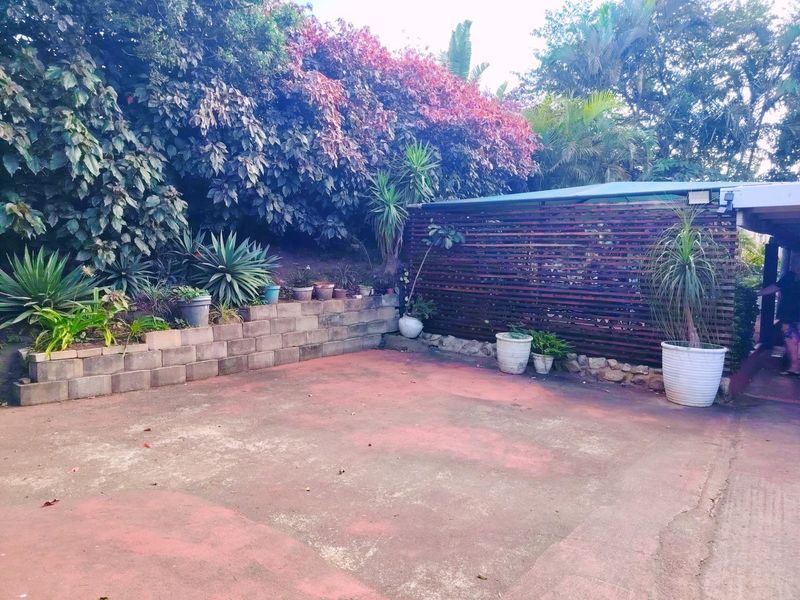 A paved outdoor patio area featuring a timber privacy screen, retaining wall, and established garden borders, offering a private space for outdoor relaxation.