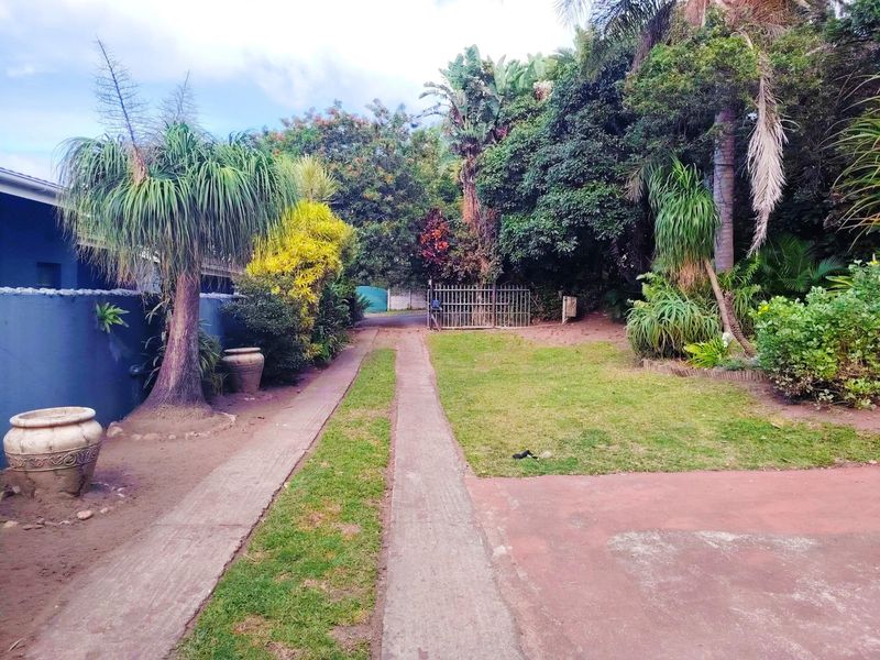 A view of the property's front entrance featuring a concrete driveway, established garden, and gated access.