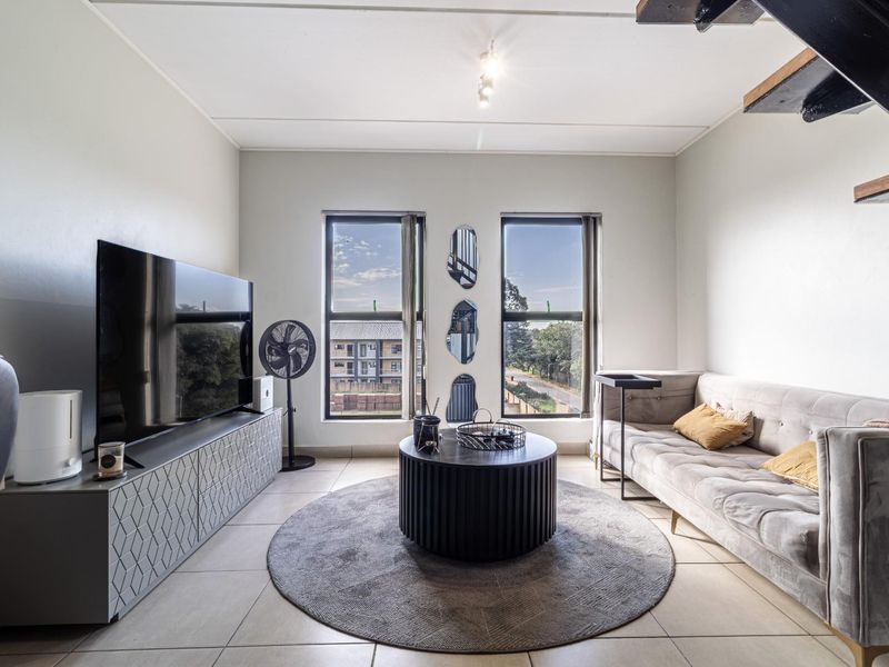 A bright and modern living room featuring large windows, tiled flooring, and a staircase leading to an upper level.