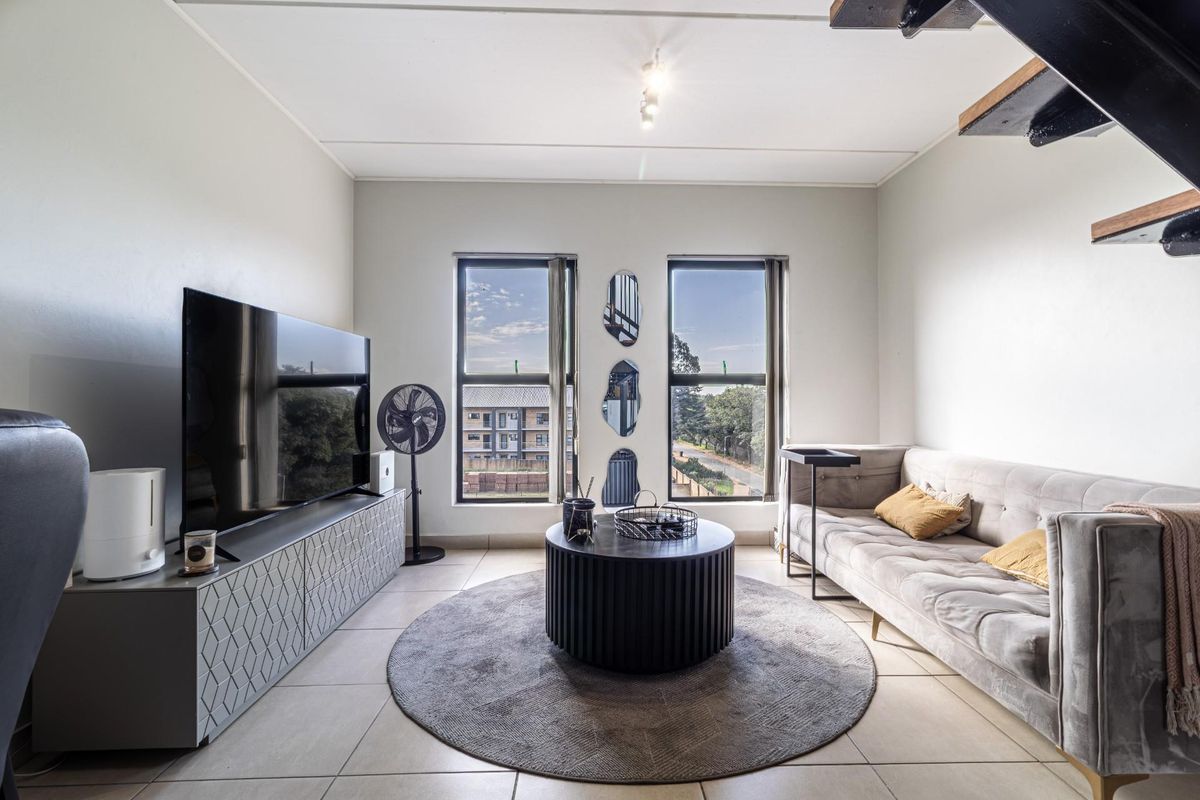 A bright and modern living room featuring large windows, tiled flooring, and a staircase leading to an upper level.