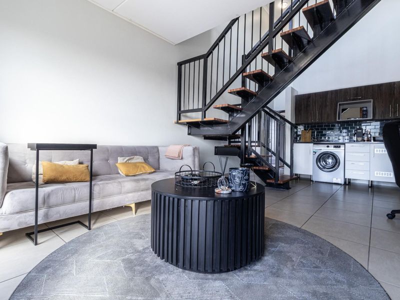 Open-plan living area featuring a modern staircase, tiled flooring, and a compact kitchen with built-in cabinetry and integrated laundry appliance.