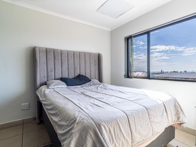 A bright bedroom featuring tiled flooring, a large window with natural light, and a ceiling access hatch.