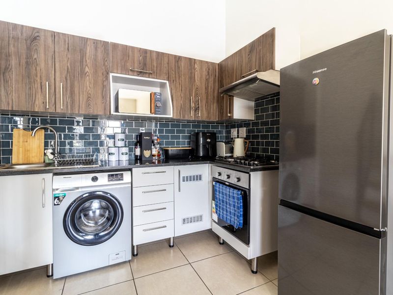 Compact kitchen featuring dark wood-grain cabinetry, subway tile backsplash, integrated oven, gas hob, extractor fan, and space for a washing machine.