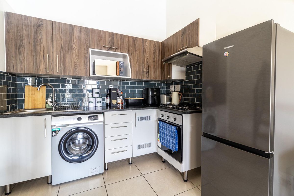Compact kitchen featuring dark wood-grain cabinetry, subway tile backsplash, integrated oven, gas hob, extractor fan, and space for a washing machine.