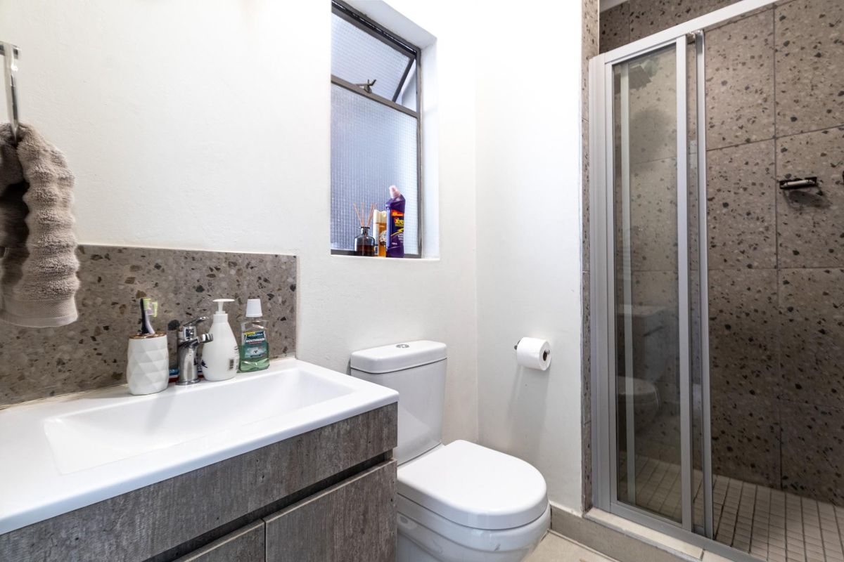A compact bathroom featuring a modern vanity with stone-look backsplash, a white toilet, and a glass-enclosed shower with textured wall tiling.