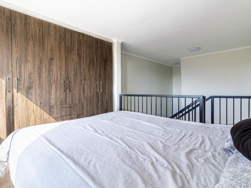 A loft-style bedroom featuring built-in wood-grain cabinetry and a black metal safety railing overlooking the lower level.