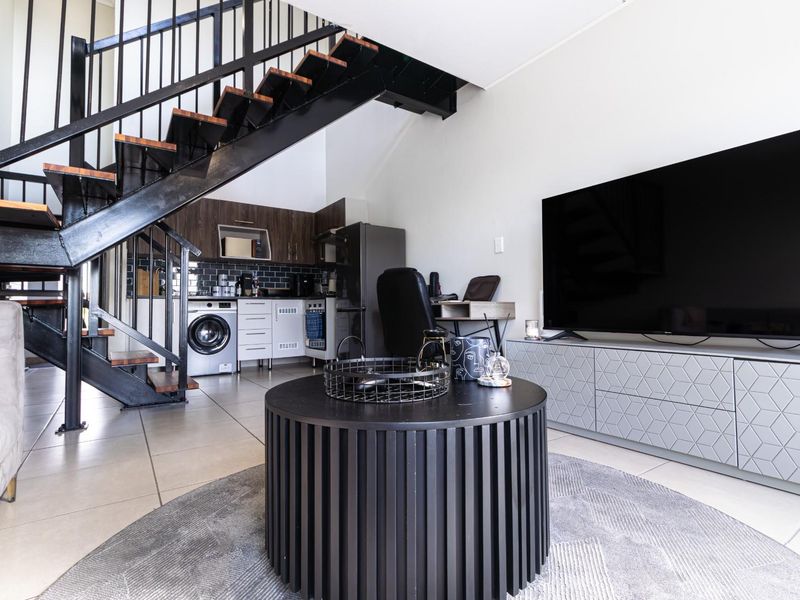 Open-plan living area featuring a modern kitchen, tiled flooring, and a striking industrial-style staircase leading to the upper level.