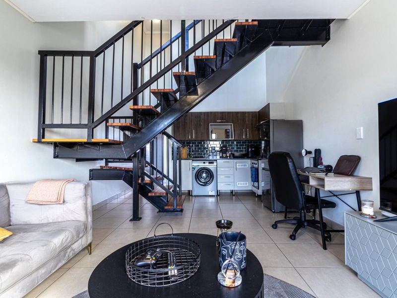 Open-plan living area featuring a modern industrial-style staircase, tiled flooring, and a compact kitchen with built-in cabinetry and integrated appliances.