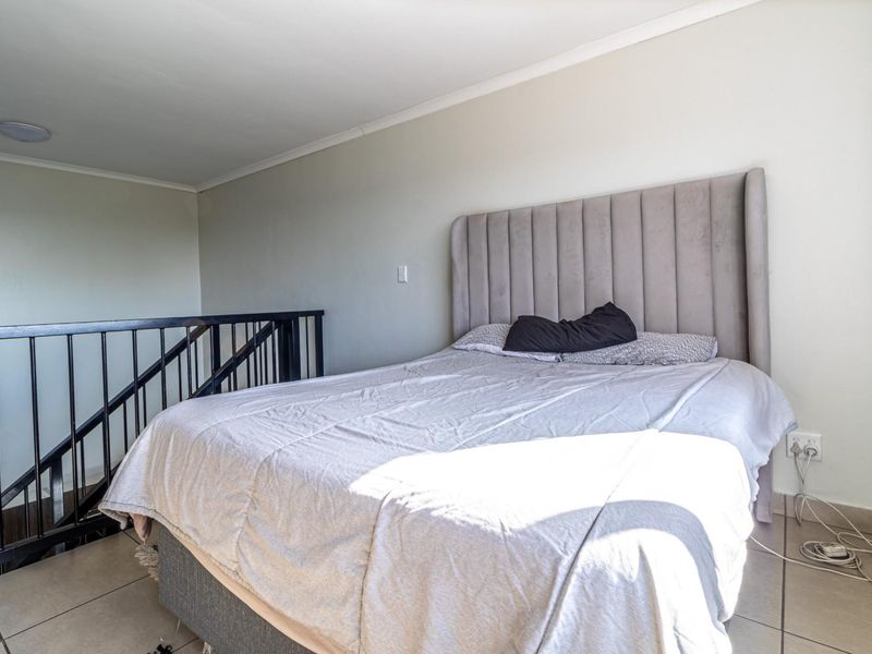 A loft-style bedroom featuring tiled flooring and a black metal safety railing overlooking the lower level.