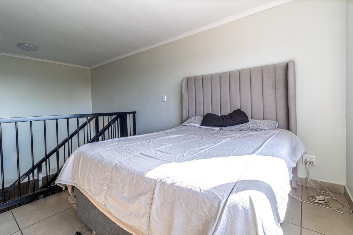 A loft-style bedroom featuring tiled flooring and a black metal safety railing overlooking the lower level.