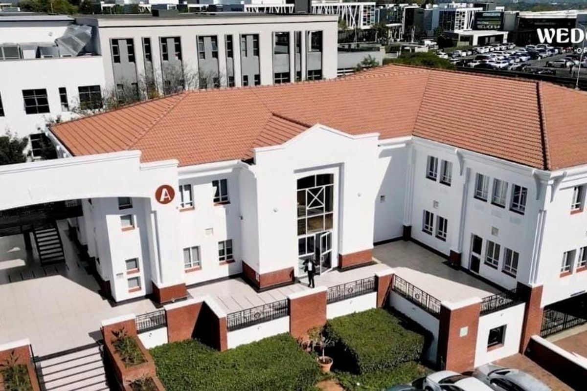 Aerial view of a commercial office building complex featuring a tiled roof, white facade with brick accents, and landscaped entrance area.