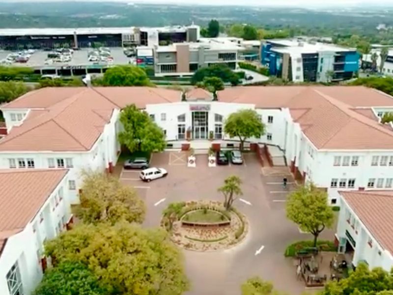 Aerial view of a commercial office complex featuring a central courtyard, paved parking area, and landscaped grounds with multiple building wings.