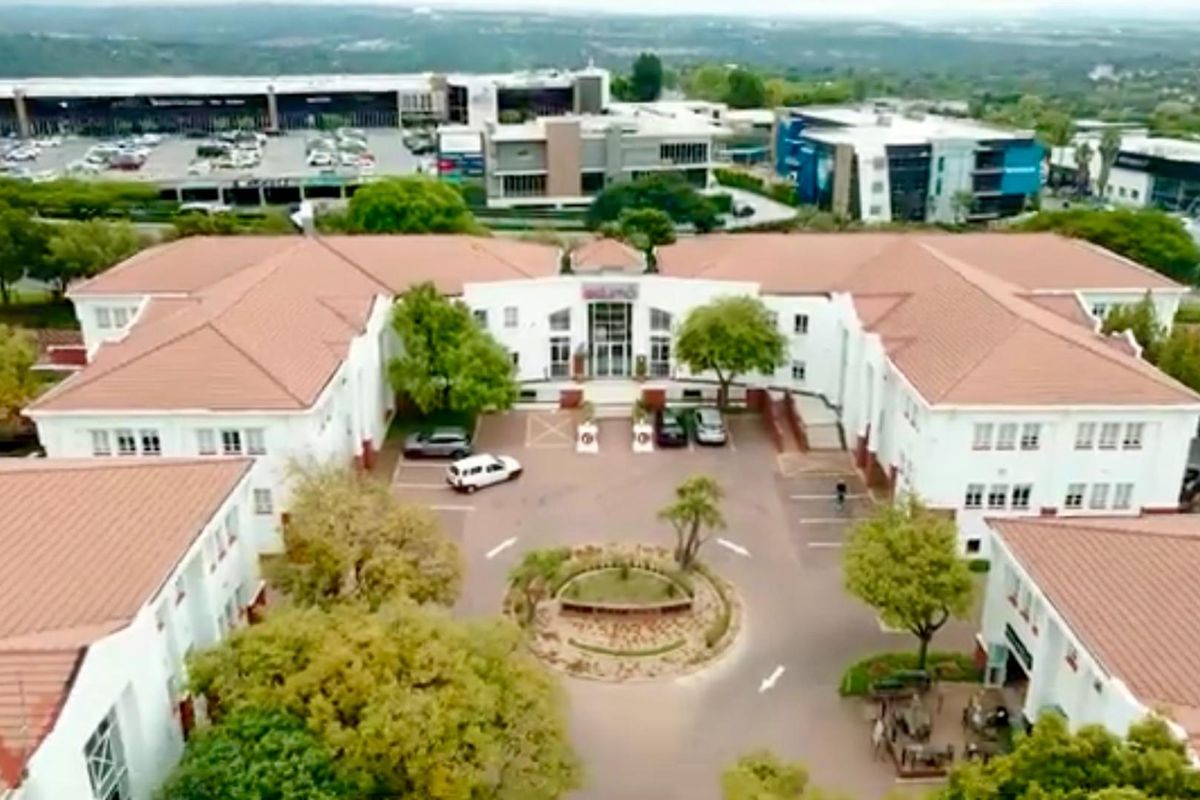 Aerial view of a commercial office complex featuring a central courtyard, paved parking area, and landscaped grounds with multiple building wings.