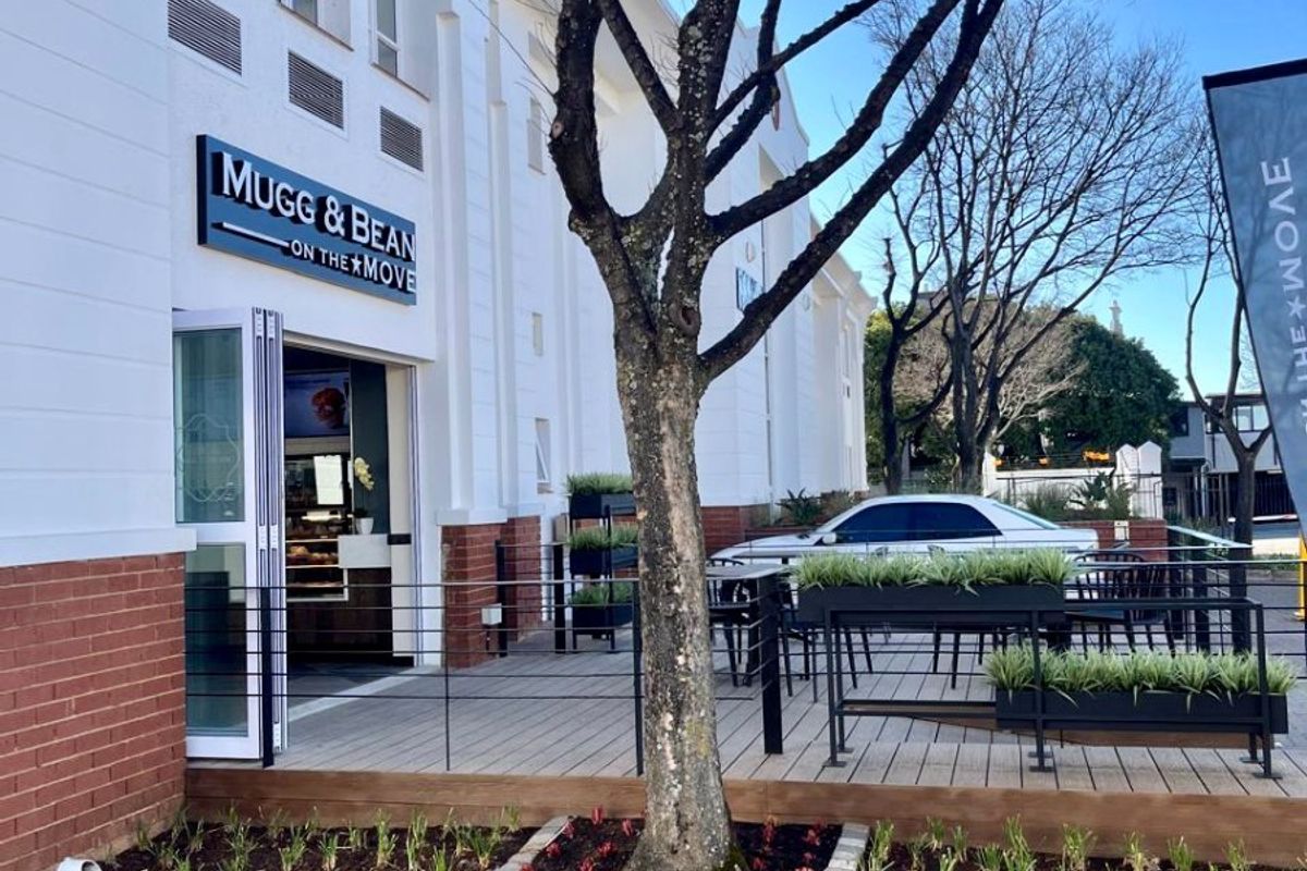 Exterior view of a commercial storefront featuring a wooden deck patio, landscaped garden beds, and modern building facade with signage.