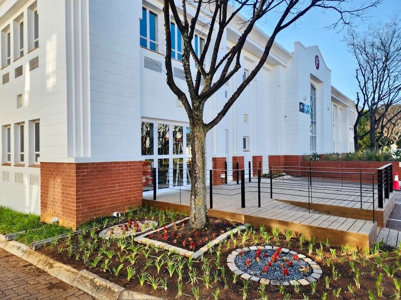 Modern commercial building exterior featuring a white facade with brick base, timber decking entrance, and landscaped garden beds.