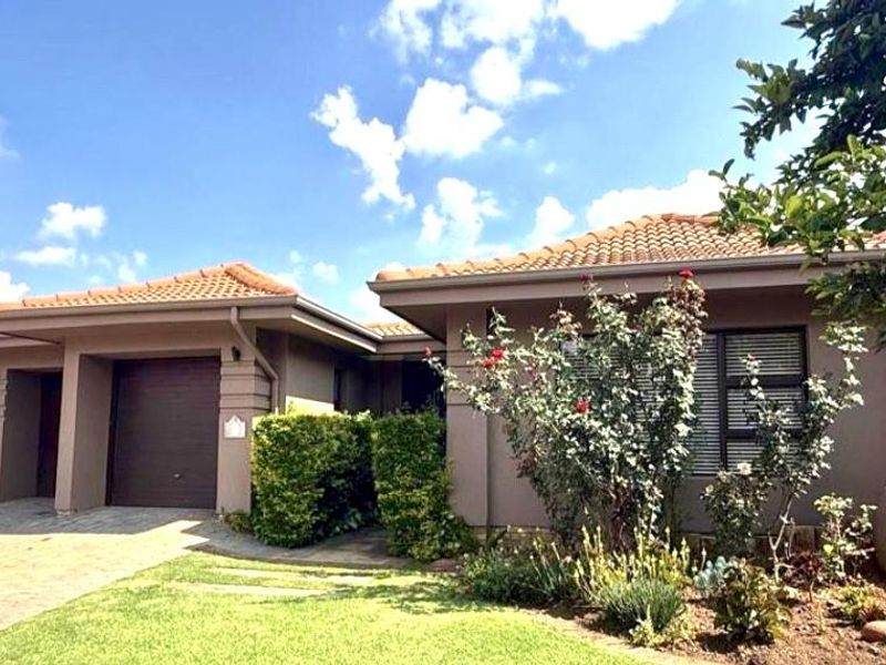 A well-maintained single-story residential home featuring a tiled roof, paved driveway, integrated garage, and established front garden landscaping.