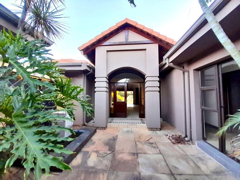 A covered entrance porch with tiled flooring and a prominent arched entryway leading into the home, set within a landscaped courtyard area.