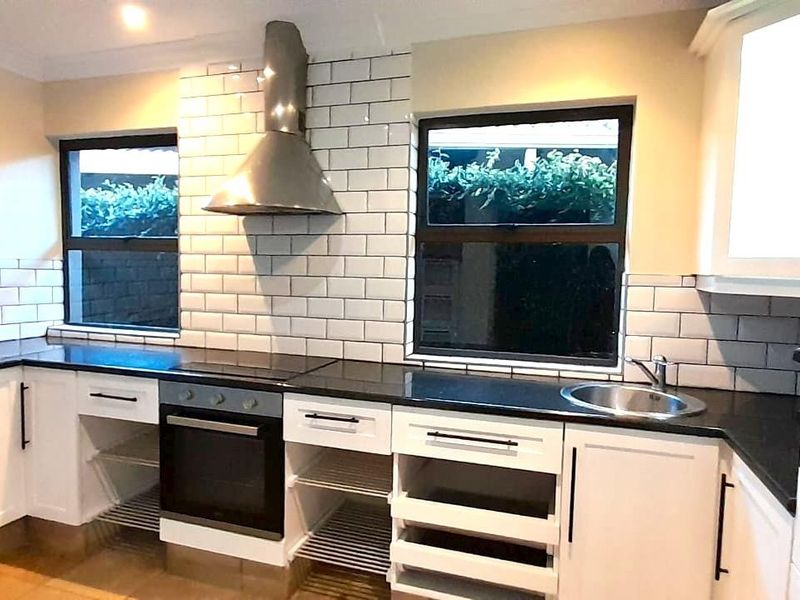 Modern kitchen featuring white cabinetry, black countertops, subway tile backsplash, stainless steel extractor fan, and built-in oven.