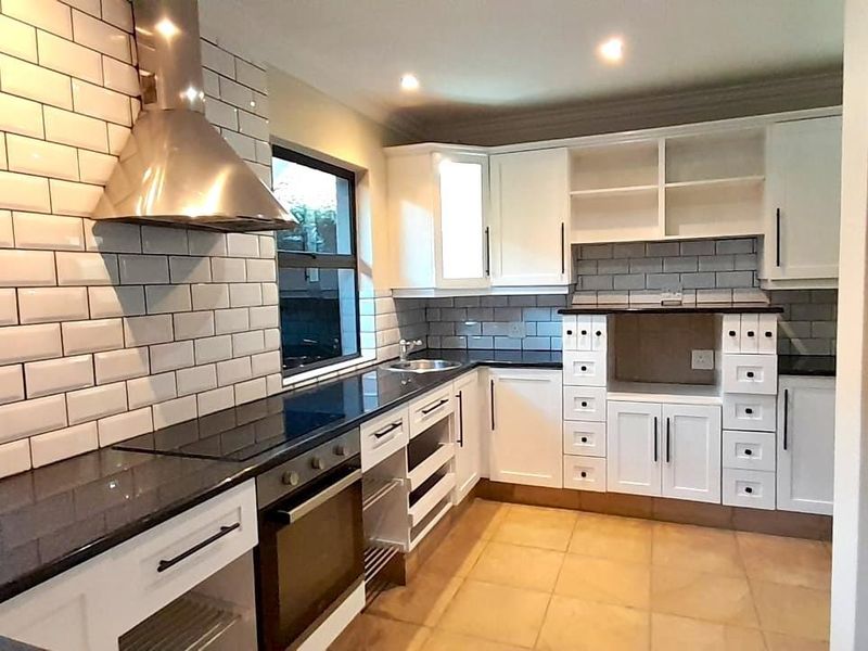 Modern kitchen featuring white cabinetry, black granite countertops, subway tile backsplash, stainless steel extractor fan, and built-in oven.