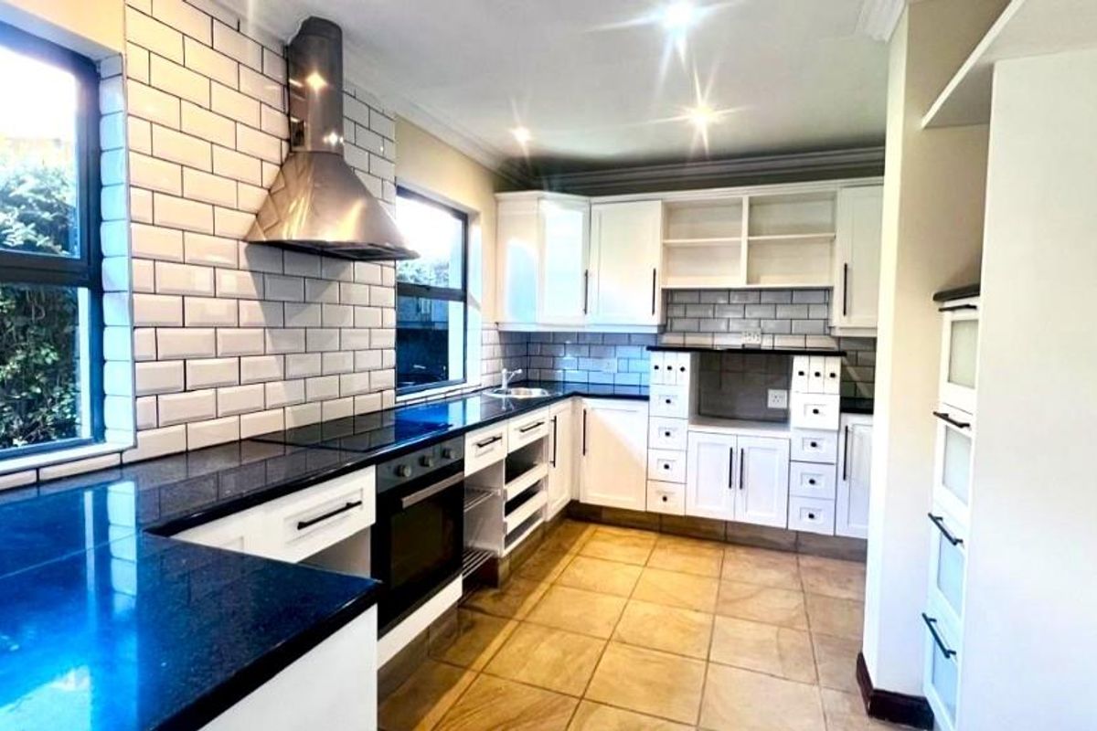 A modern kitchen featuring white cabinetry, dark granite countertops, subway tile backsplash, and a stainless steel extractor fan.