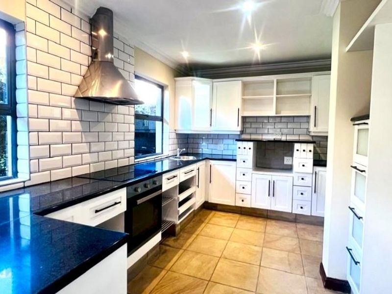 A modern kitchen featuring white cabinetry, dark granite countertops, subway tile backsplash, and a stainless steel extractor fan.