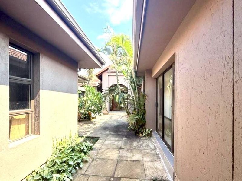 A paved walkway between two sections of the house, featuring exterior walls and access to a landscaped garden area.