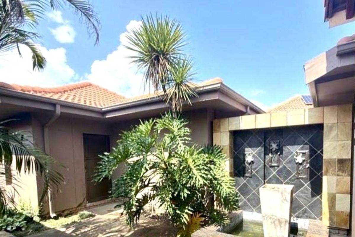 A well-maintained exterior courtyard area featuring a decorative tiled water feature, established landscaping, and terracotta roof tiles.