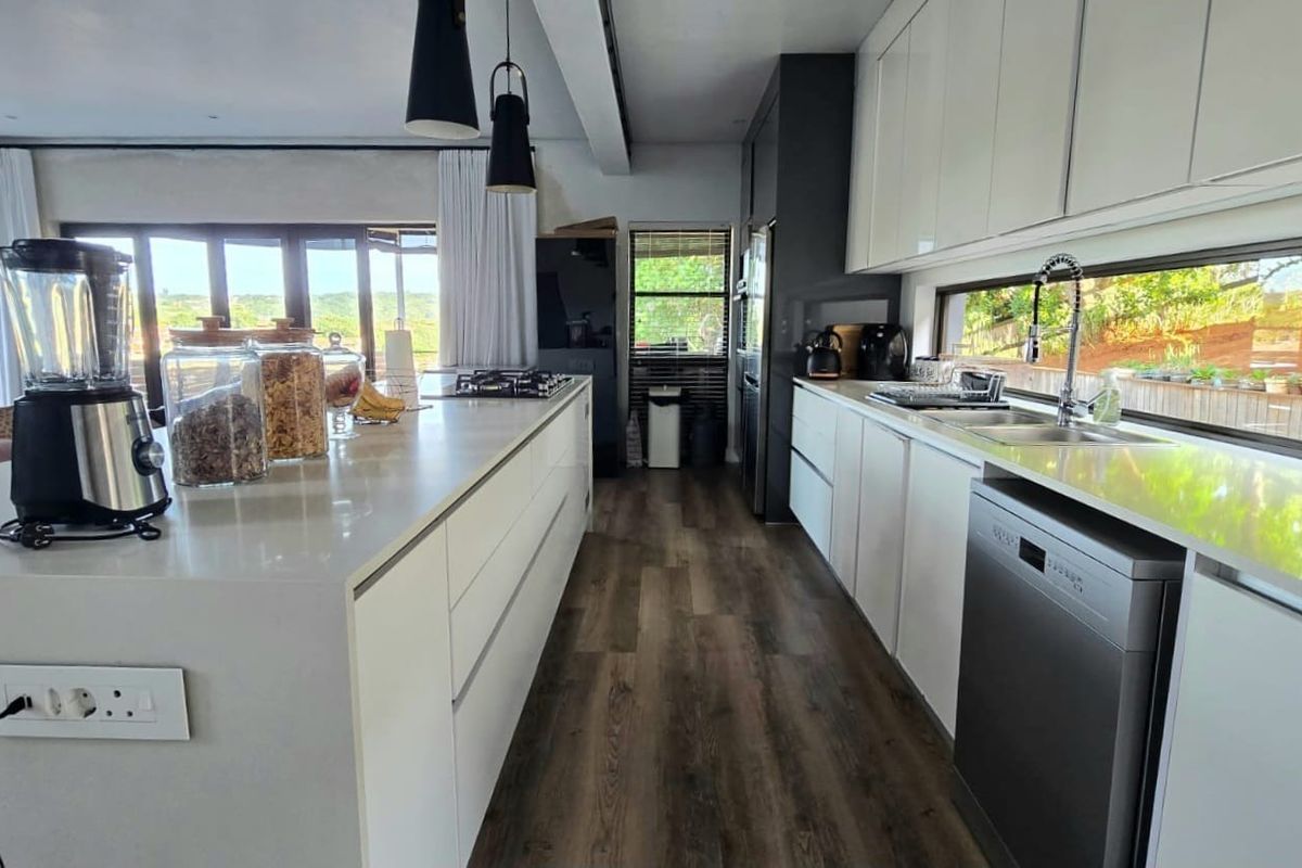 Modern kitchen featuring a large central island, sleek white cabinetry, integrated appliances, and a long horizontal window overlooking the garden.
