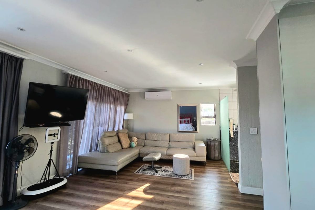 Spacious living area featuring wood-look flooring, recessed ceiling lighting, and a wall-mounted air conditioning unit, with an adjacent semi-open bathroom space.