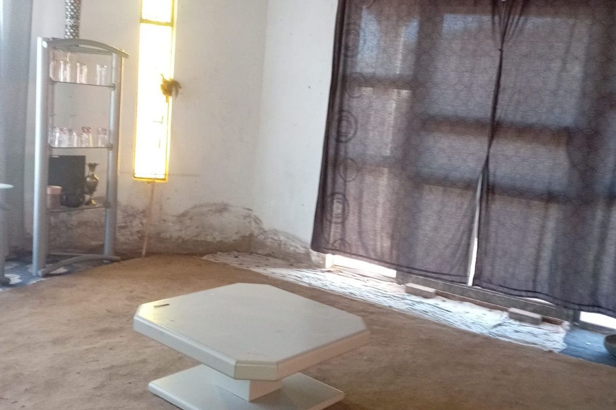 A living room space featuring exposed ceiling beams, wall dampness, and unfinished plasterwork, requiring significant renovation and repair to restore the interior finishes.