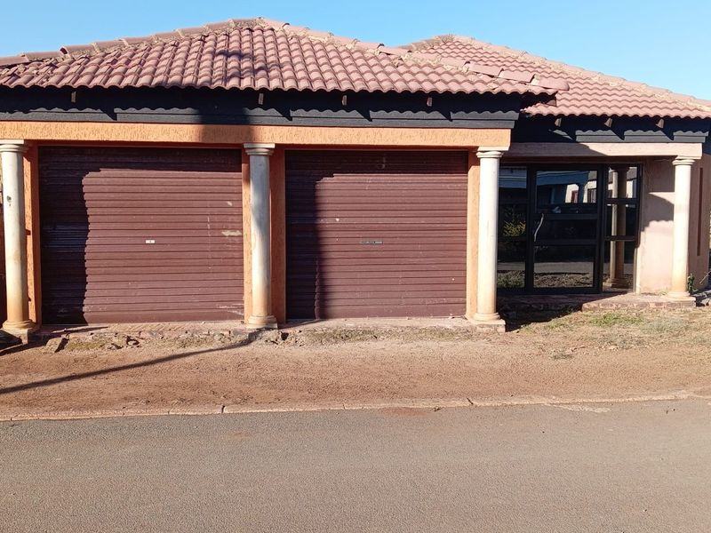 Front elevation of a residential property featuring a double garage with roller shutter doors, decorative columns, and a tiled roof.