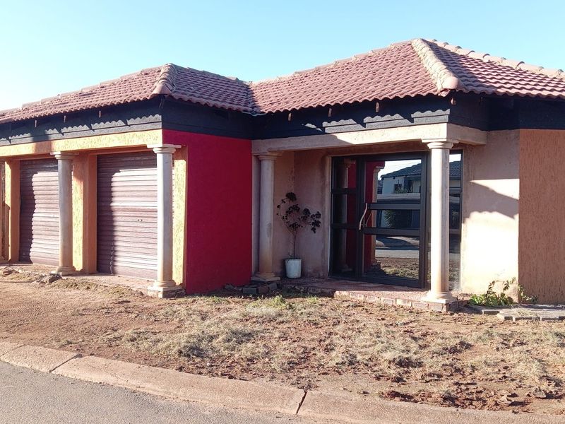 Front elevation of a single-story house featuring a double garage, decorative columns, and a tiled roof, set on an unlandscaped plot.