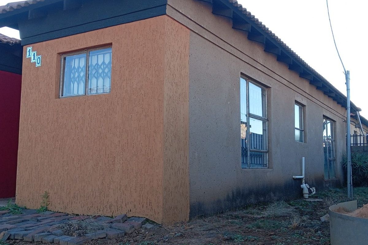 Side view of the house exterior featuring textured walls, tiled roof, and security bars on windows, set on an unlandscaped plot.