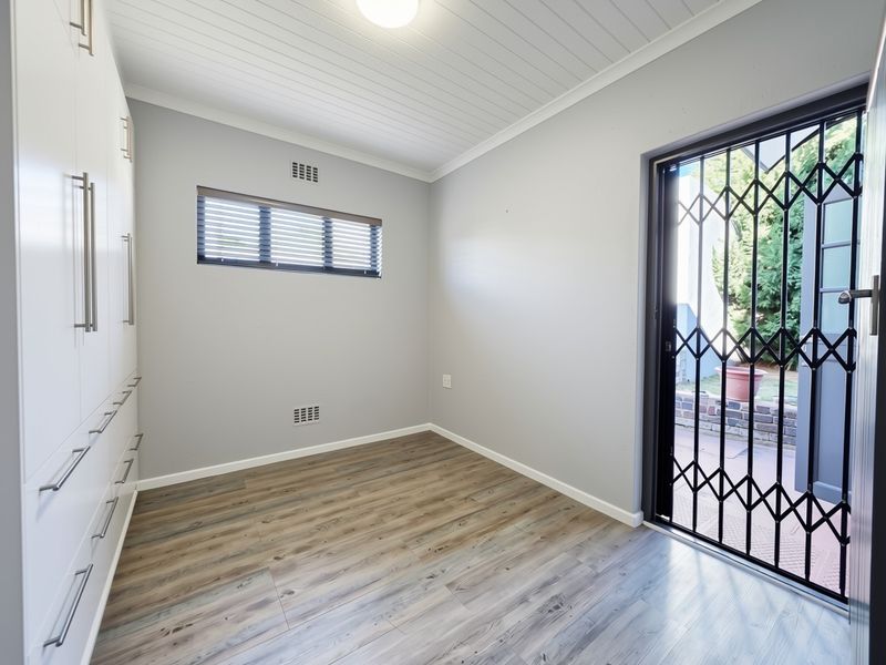 A bright, empty bedroom featuring modern laminate flooring, built-in cupboards, a tongue and groove ceiling, and a security gate leading to the exterior.