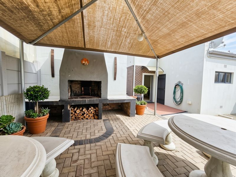 Outdoor patio area featuring a built-in braai, paved flooring, and a shade sail, providing a functional space for outdoor entertaining.