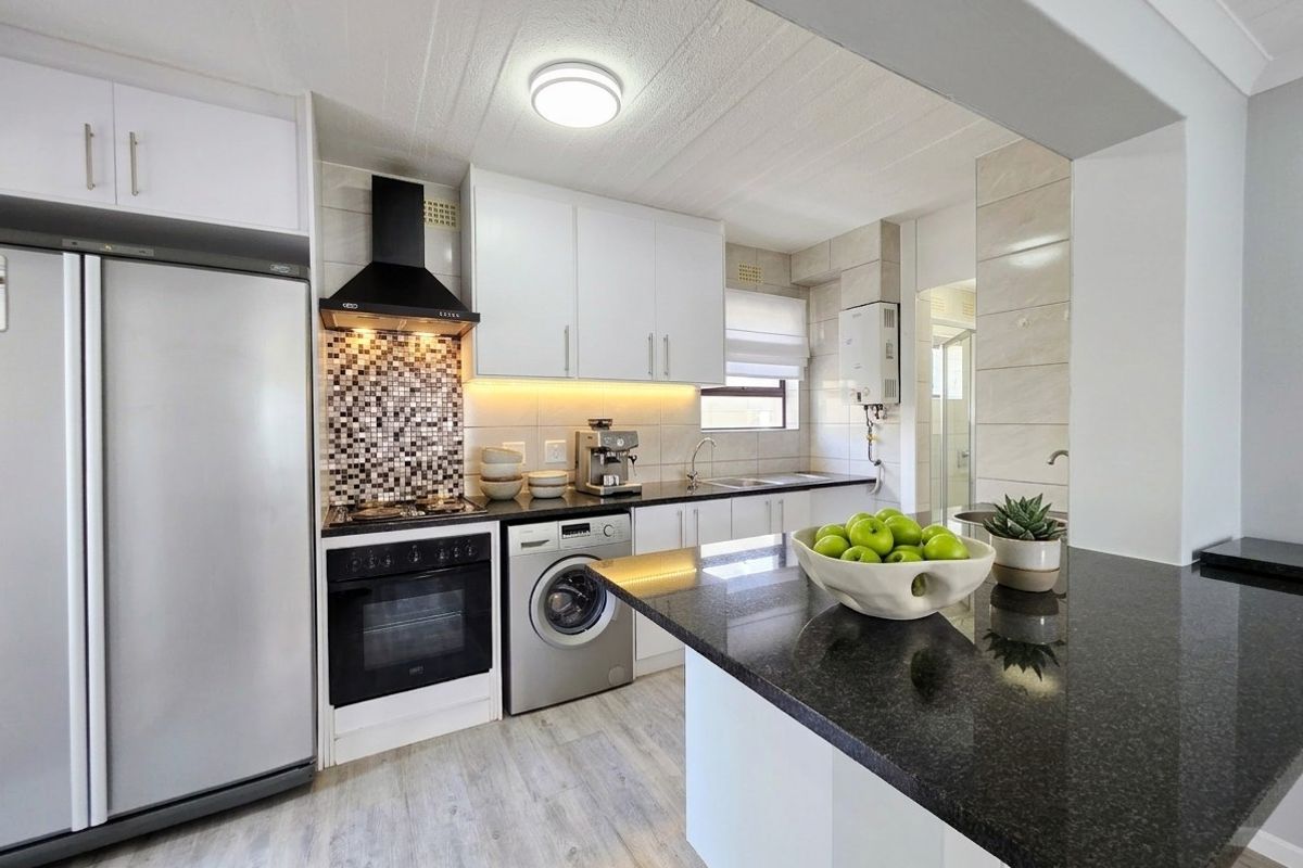 Modern kitchen featuring sleek white cabinetry, dark granite countertops, a gas stove with extractor, and integrated laundry plumbing.