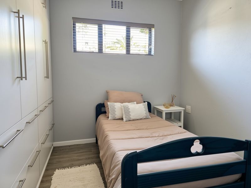 A well-maintained bedroom featuring modern laminate flooring, neutral wall tones, and extensive built-in cupboard storage with sleek hardware.