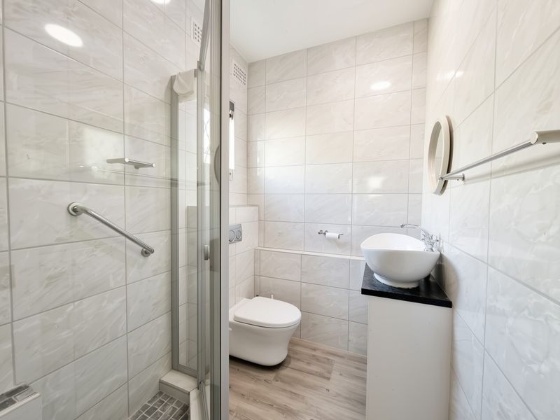Modern bathroom featuring a walk-in shower, wall-mounted toilet, and a stylish vessel sink set on a vanity cabinet with neutral wall tiling.