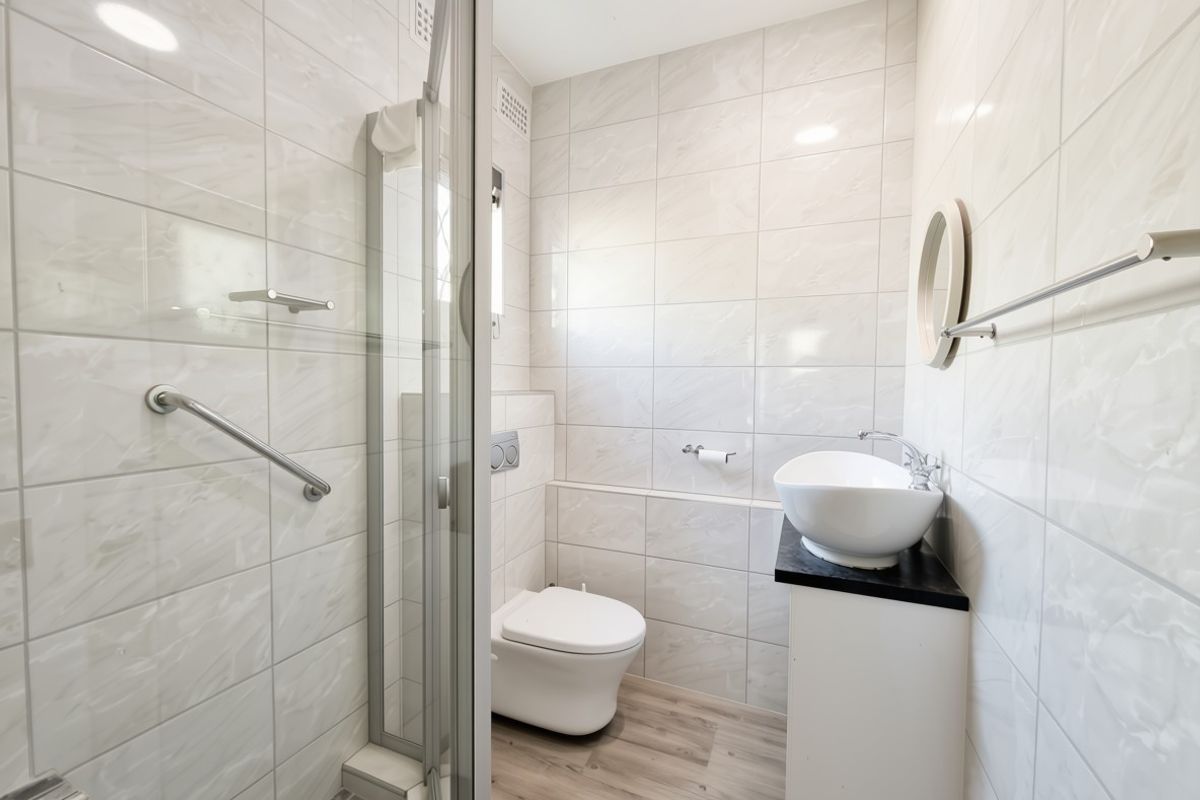 Modern bathroom featuring a walk-in shower, wall-mounted toilet, and a stylish vessel sink set on a vanity cabinet with neutral wall tiling.