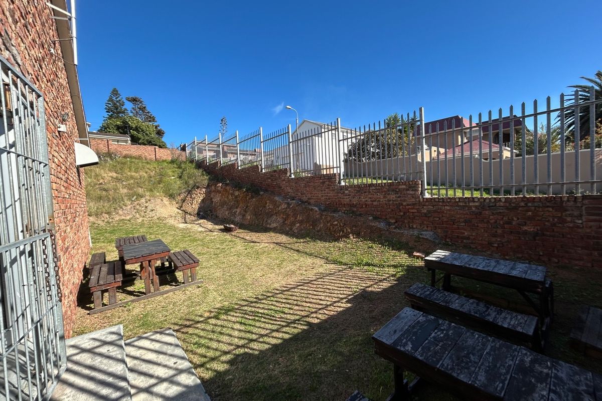 A rear outdoor garden area featuring a terraced brick retaining wall, perimeter steel security fencing, and a grassed lawn space.